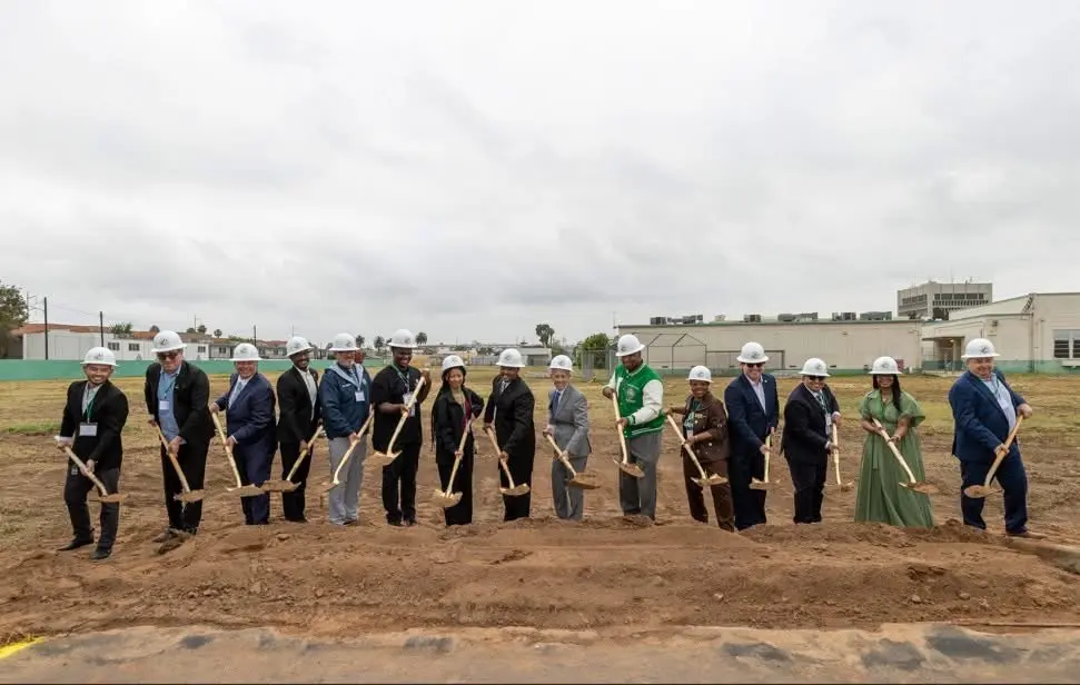 Community leaders and officials at a groundbreaking ceremony wearing hard hats and holding shovels