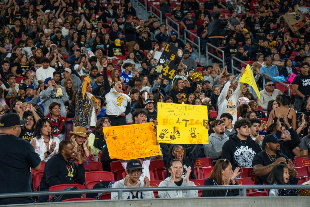 Football fans cheering at a stadium with signs, showing excitement and team spirit during a game.