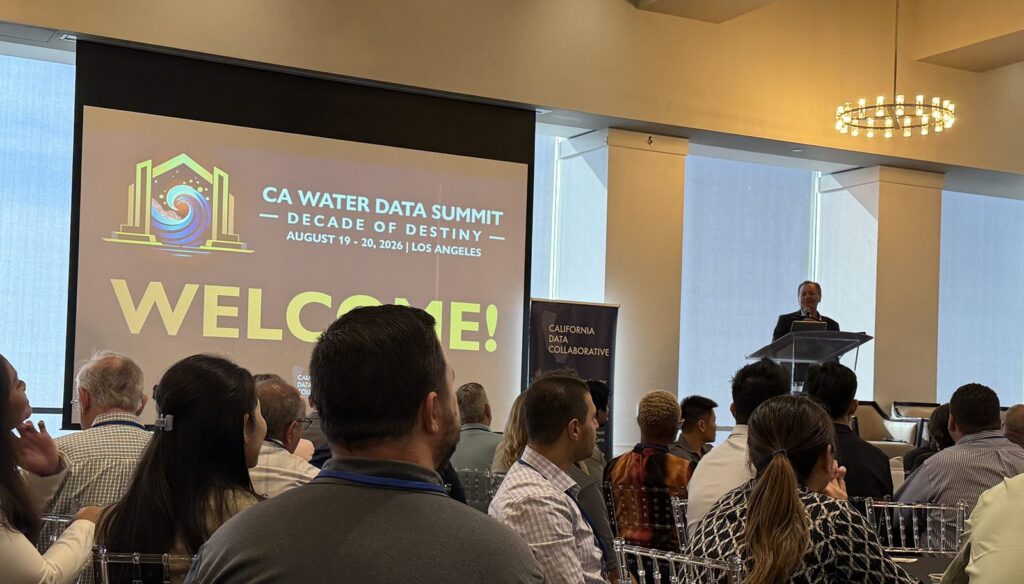 George L. Pla speaks from a podium at the 11th Annual CA Water Data Summit in Los Angeles, with the summit's Decade of Destiny welcome slide projected behind the audience.